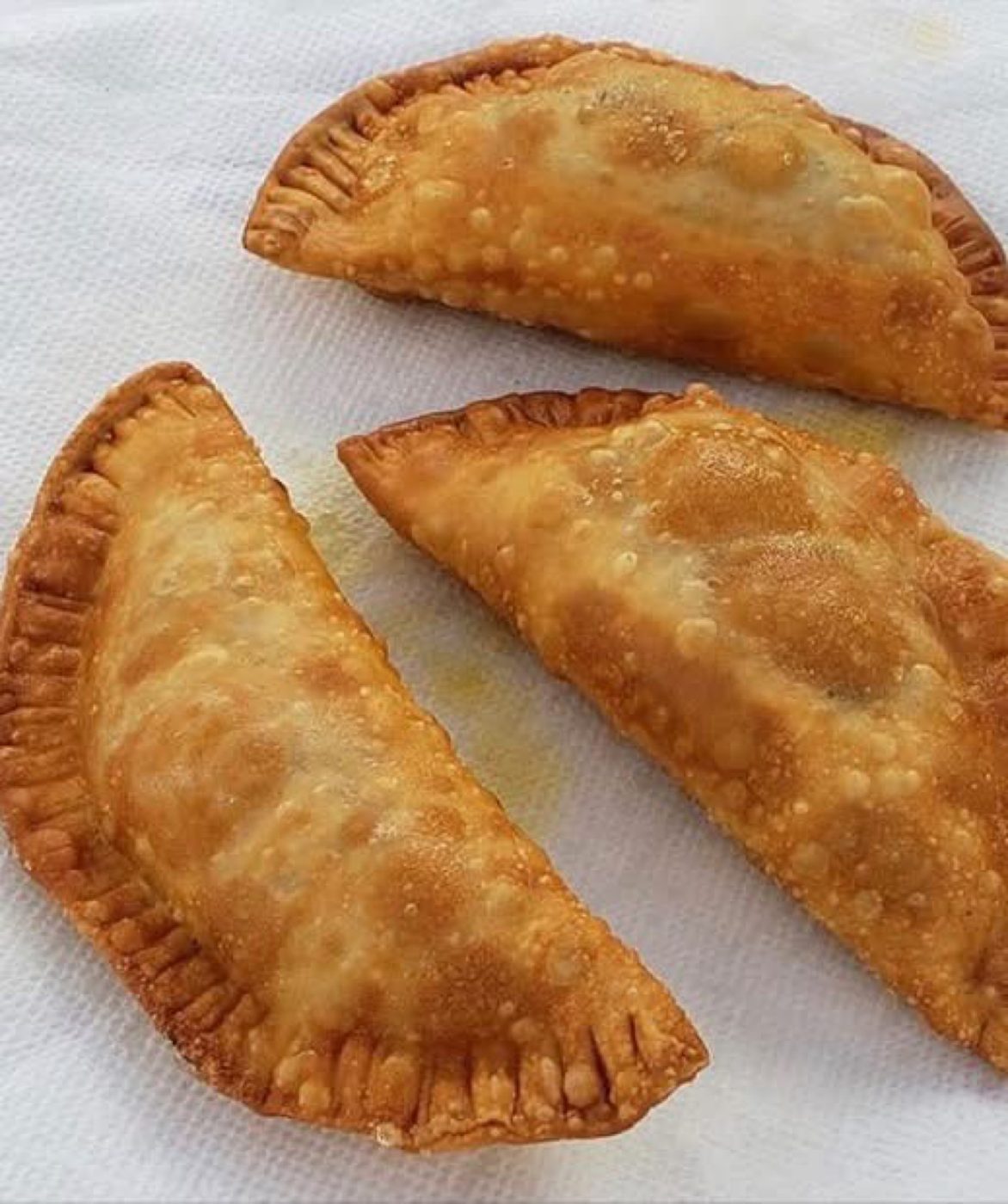 Three golden fried empanadas with crimped edges on a paper towel
